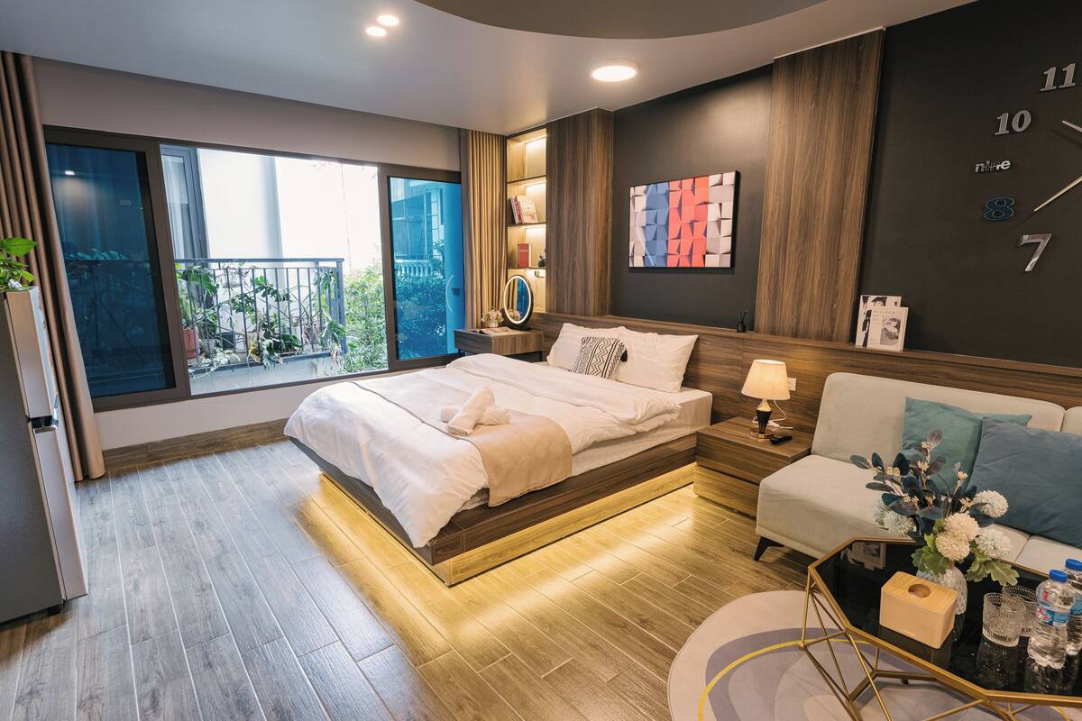 A modern bedroom with a large bed, a sofa, a coffee table, and a view of a balcony.