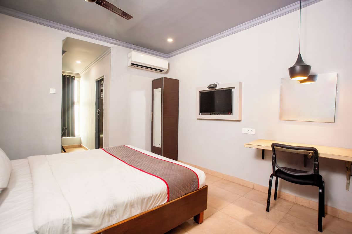 Une chambre avec un lit, un bureau, une chaise, un climatiseur et un téléviseur.