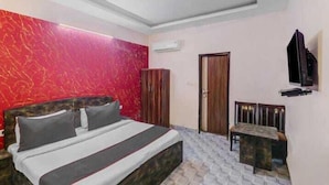 A bedroom with a bed, a wooden wardrobe, a television mounted on the wall, and a small table with chairs. - Hotel SkyView (New Delhi)