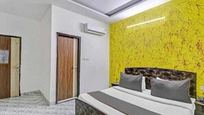 A bedroom with a bed, a wooden door, and a wall with a yellow pattern. - Hotel SkyView (New Delhi)