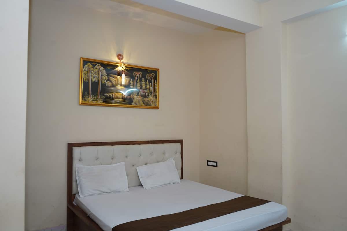 A neatly made bed with a wooden headboard and white bedding, a framed painting above it, and a light switch on the wall.
