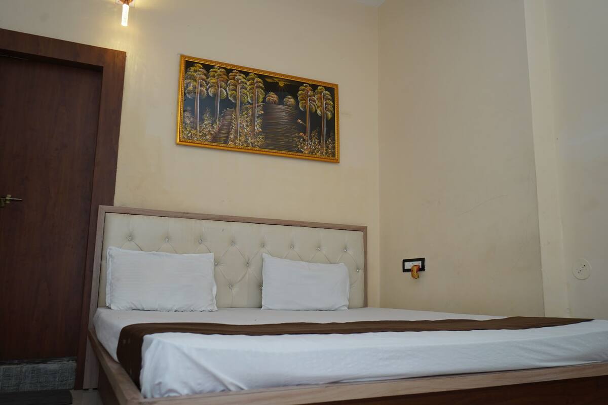 A neatly made bed with a wooden headboard and white bedding, a wooden door to the left, and a framed painting above the bed.