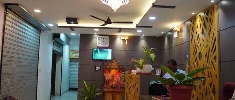 A hotel reception area with a ceiling fan, a clock, and a television on the wall.