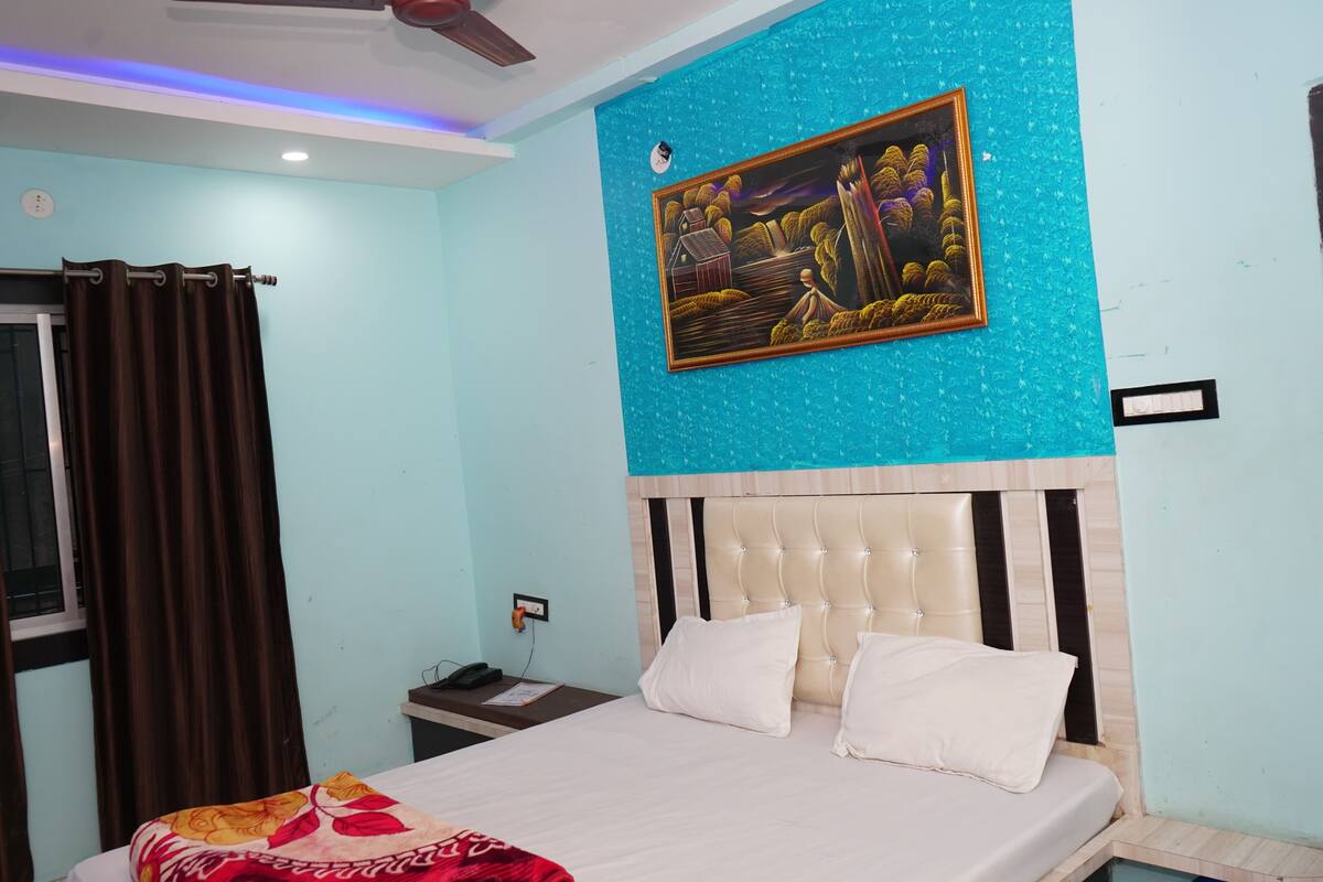 A bedroom with a bed, a nightstand, a painting, and a window with curtains.