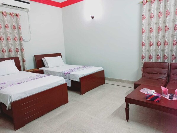A hotel room with two single beds, a wooden table with a remote control, and a red sofa. - Gulshan Family Guest House  (Karachi)