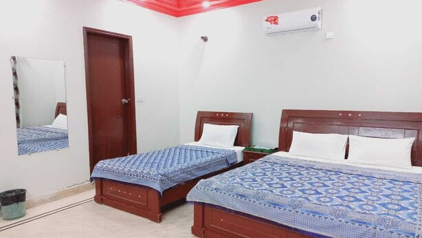 A room with two wooden beds, a ceiling fan, a wall-mounted air conditioner, and a door. - Gulshan Family Guest House  (Karachi)