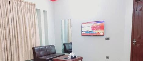 A family guest house with a sofa, a small table, a TV mounted on the wall, and a red door.