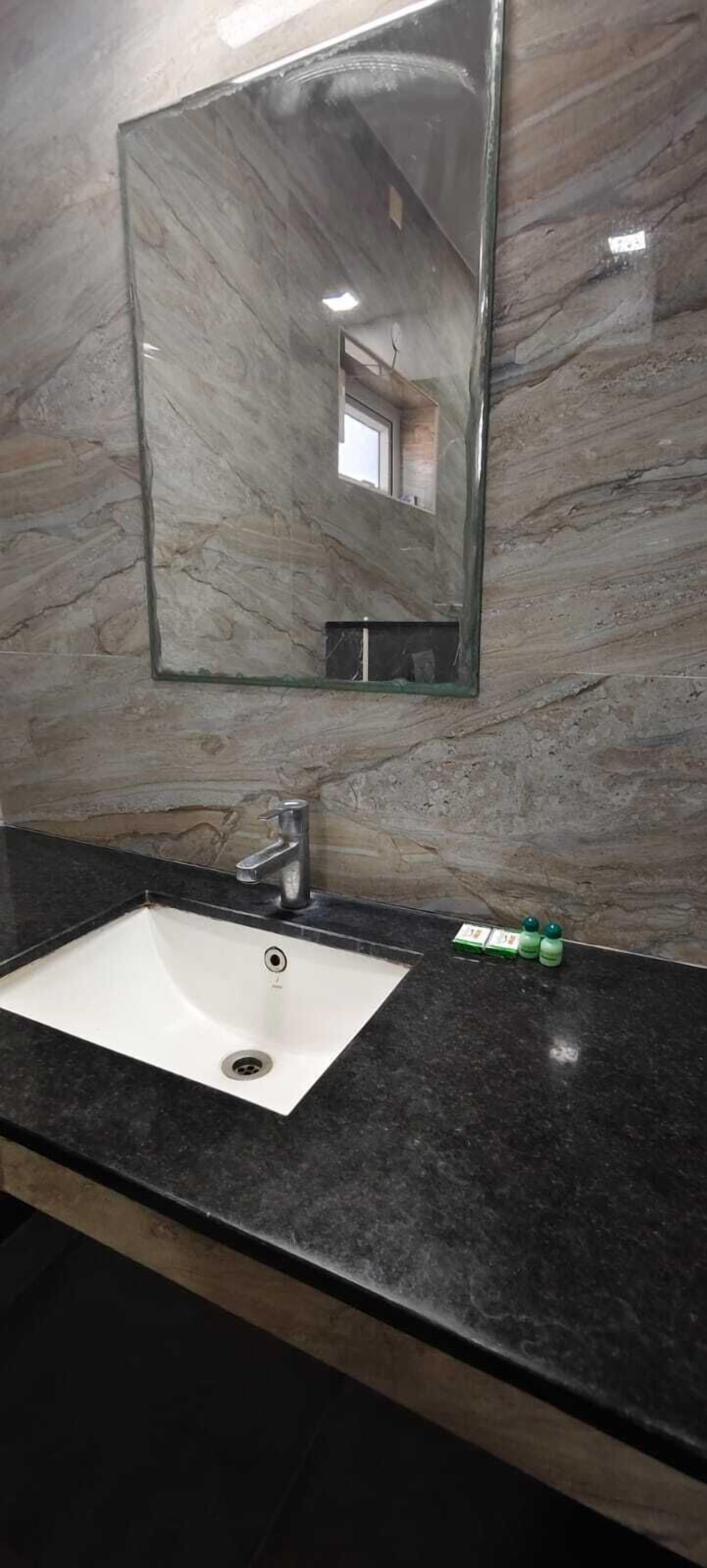 Een badkamer met een marmeren wand, een wit wastafelmeubel en een spiegel.