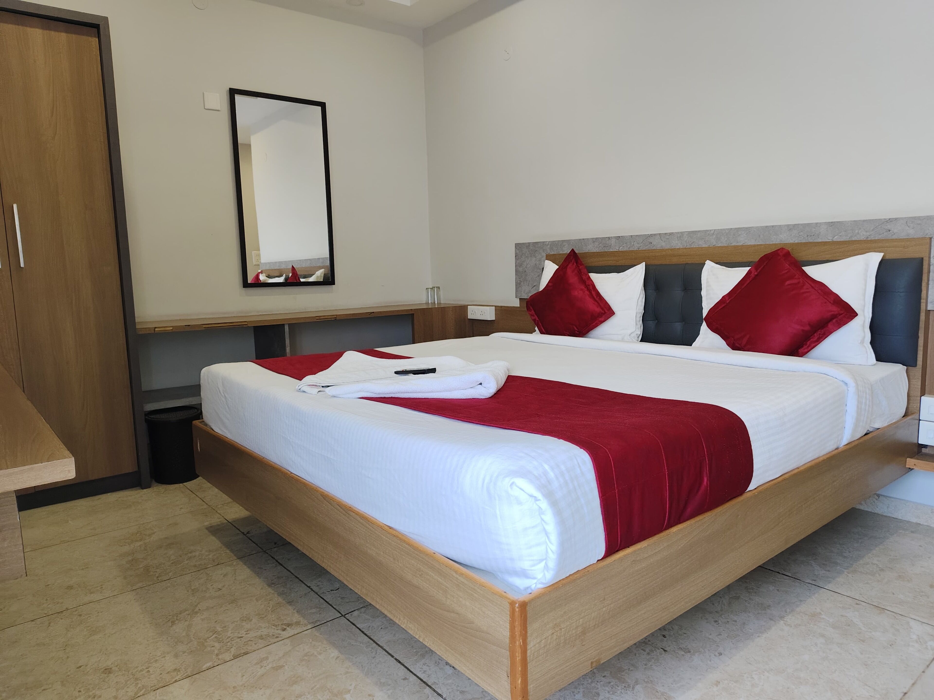 A neatly made bed with a wooden frame and white bedding, red pillows, and a red throw blanket.