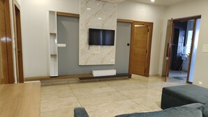 Una sala de estar moderna con un televisor de pantalla plana montado en una pared de mármol, una puerta de madera y suelo de baldosas.