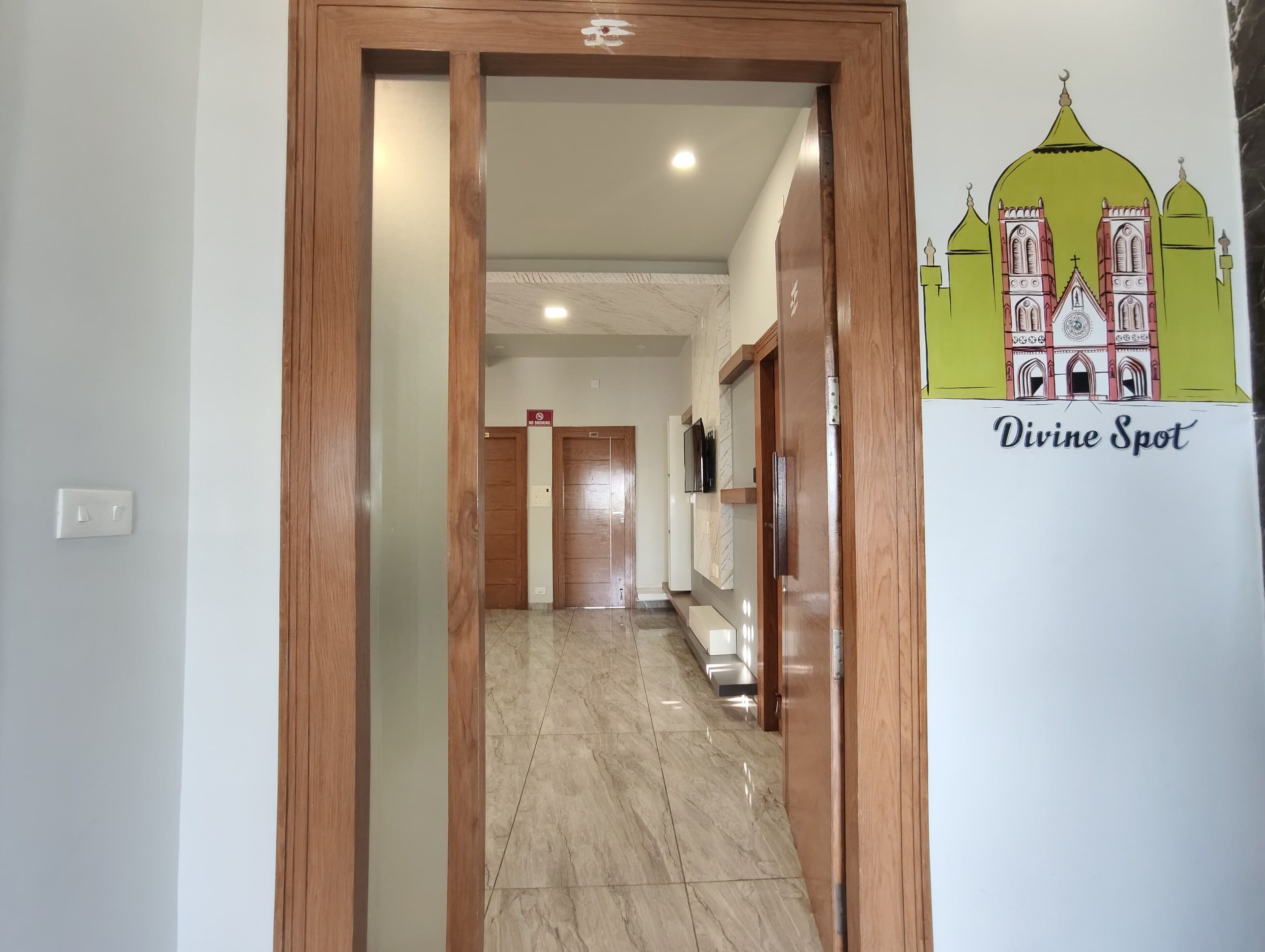Un couloir avec des portes en bois, un sol carrelé et un mur sur lequel est affiché un panneau indiquant « Divine Spot ».