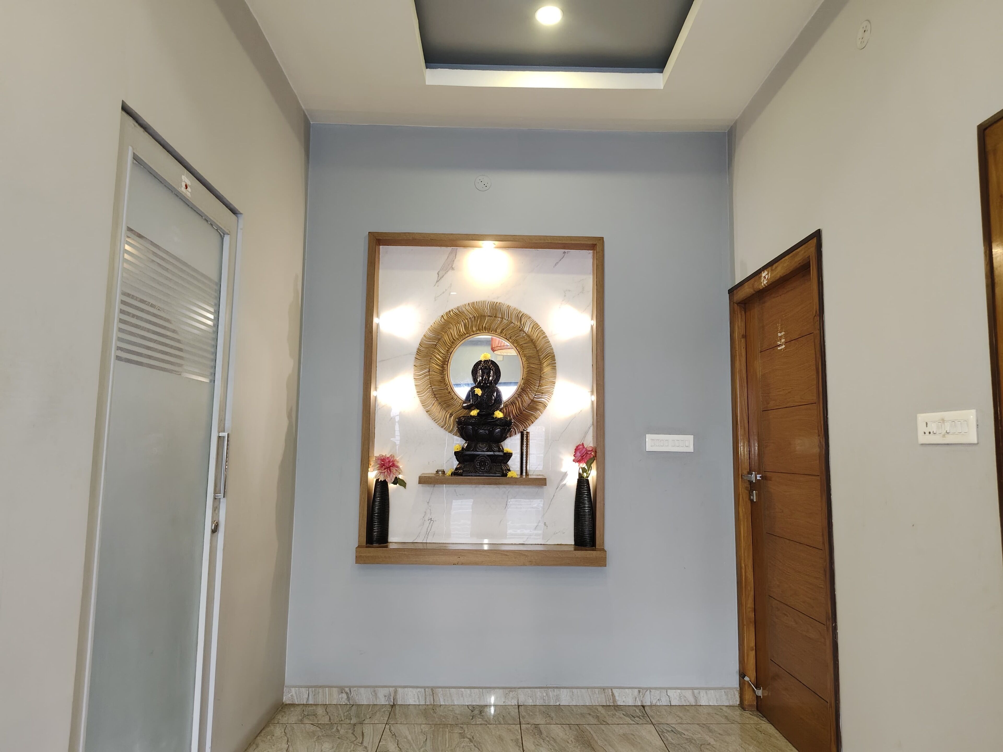 A hallway with a ceiling light, a wooden door, and a wall-mounted mirror with a decorative frame.