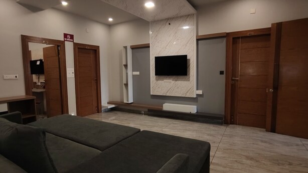 Una sala de estar moderna con un sofá gris, puertas de madera, un televisor montado en la pared y un letrero que indica 'No Smoking'.