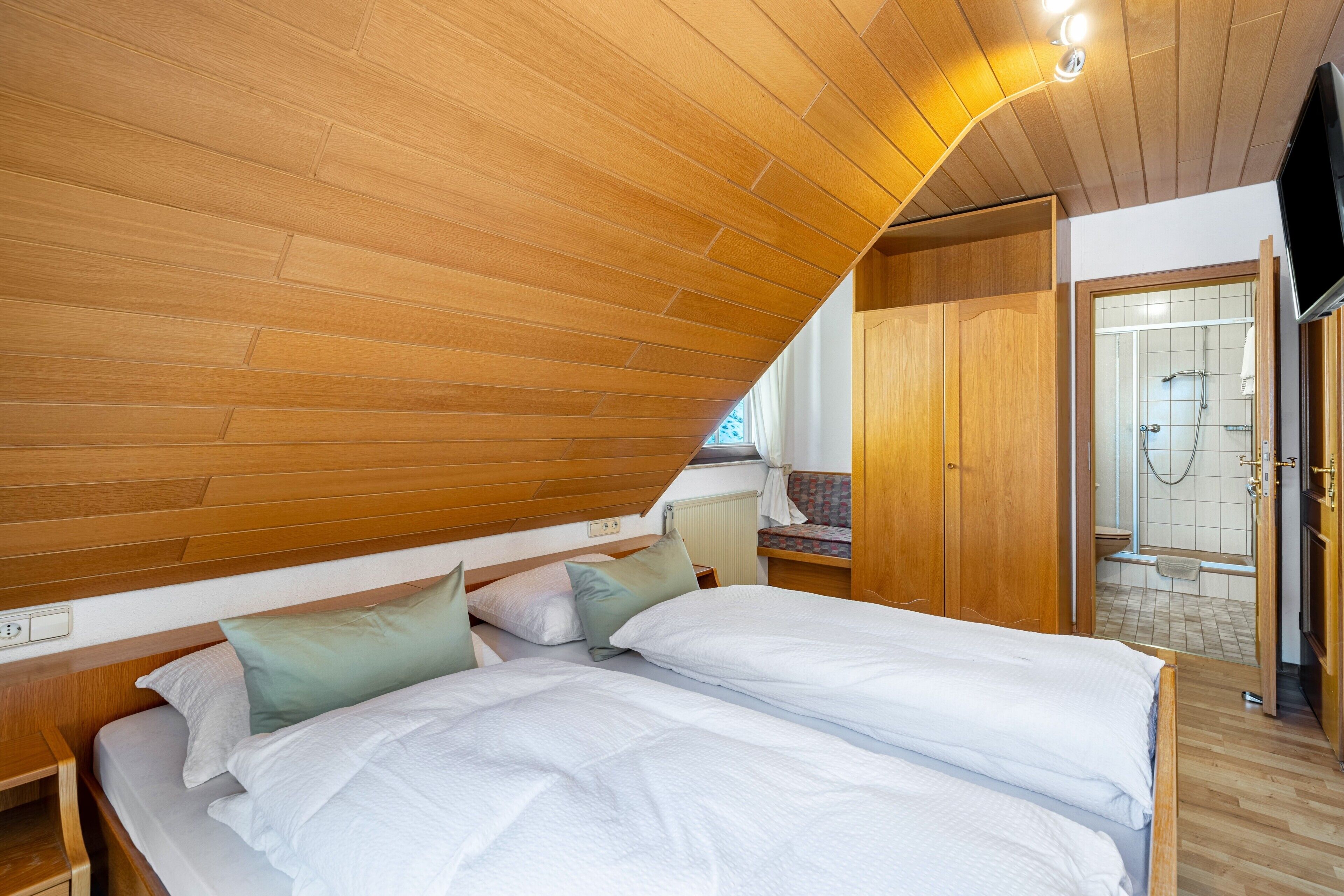Une chambre avec un plafond en bois, un lit avec une literie blanche, une armoire en bois et un espace douche.