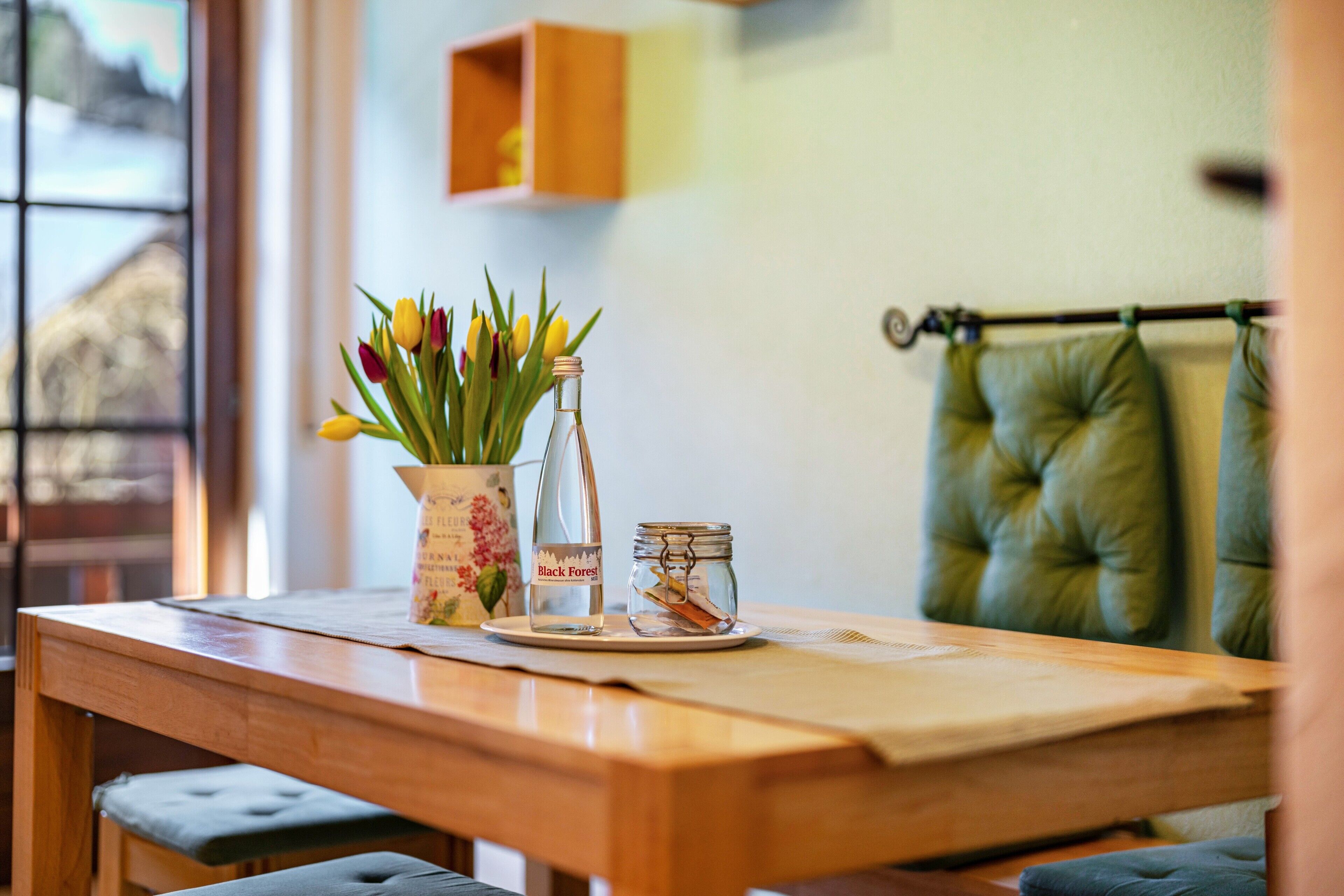 Una mesa de madera con un jarrón de tulipanes, una botella de vidrio y un frasco pequeño.