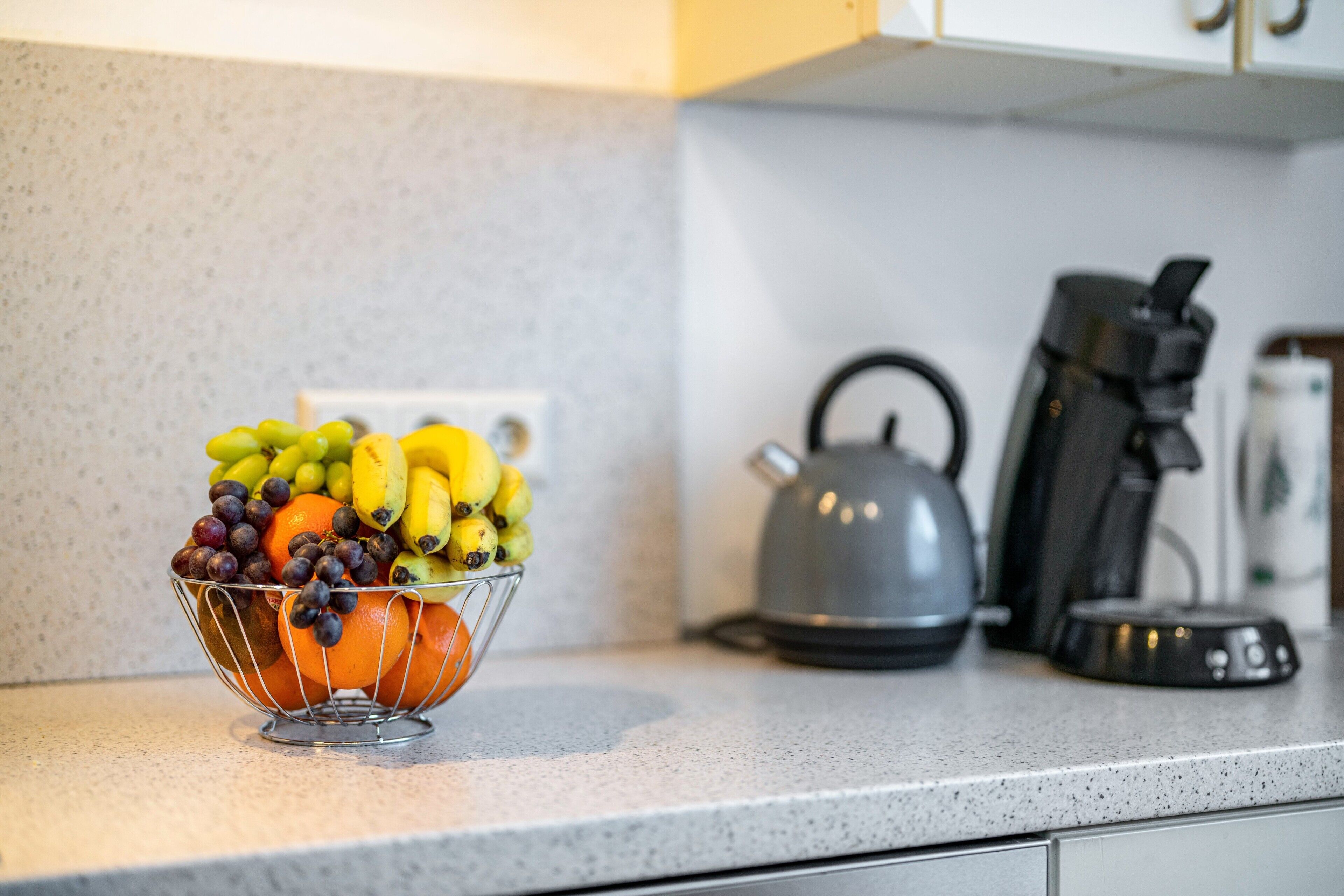 Un comptoir de cuisine sur lequel se trouve un panier de fruits contenant des raisins, des bananes et des oranges.