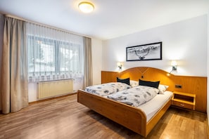 Un dormitorio con cama de madera, un radiador, una ventana con cortinas e imagen colgada en la pared.