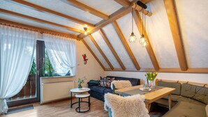 A cozy room with a wooden ceiling, a sofa, a table, and a chair. - Apartment '6' with Mountain View, Shared Terrace and Wi-Fi (Bad Rippoldsau-Schapbach)