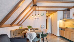 A cozy loft-style room with a dining area, a sofa, and a kitchen with wooden cabinets and a dishwasher. - Apartment '6' with Mountain View, Shared Terrace and Wi-Fi (Bad Rippoldsau-Schapbach)