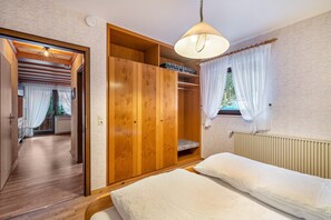 A bedroom with a bed, wooden wardrobe, and a window with curtains. - Apartment '6' with Mountain View, Shared Terrace and Wi-Fi (Bad Rippoldsau-Schapbach)