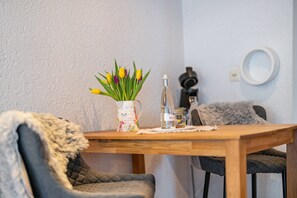 A wooden dining table with a vase of flowers, a bottle, and a small jar. There are two chairs with fur throw blankets.