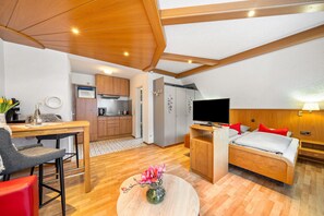 A compact room with a bed, a TV, a dining area, and a kitchenette.