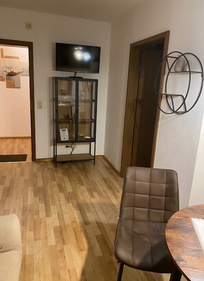 Un salon avec un plancher en bois, un téléviseur fixé au mur, une vitrine et un fauteuil en cuir marron.
