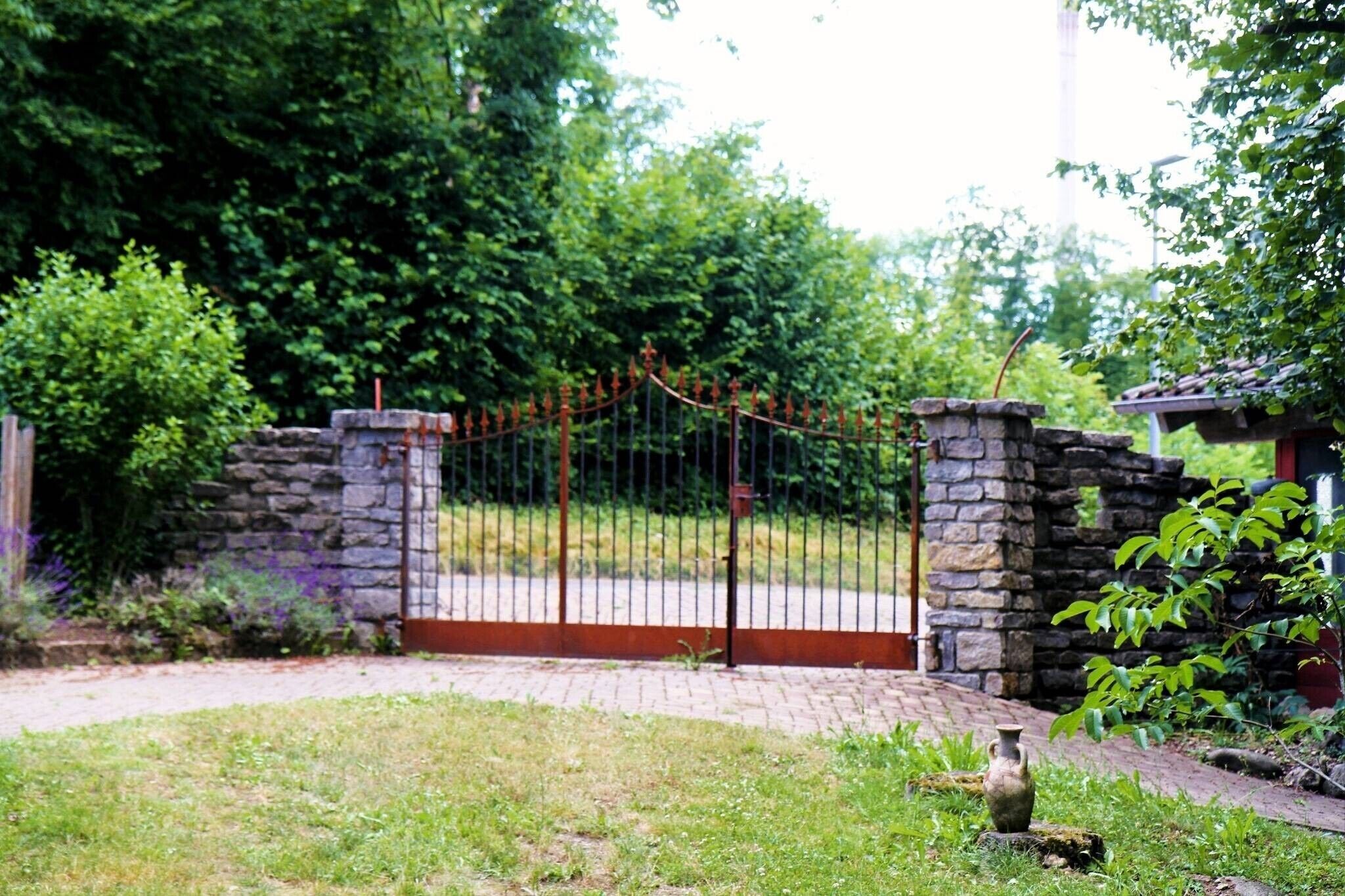 Une entrée fermée par un portail, avec des murs en pierre, un chemin pavé et une petite construction dotée d’un toit.