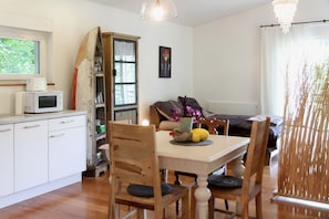 A dining area with a wooden table, chairs, a vase with flowers, and a microwave on the counter.