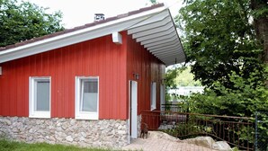 Un bâtiment rouge avec des fondations en pierre, un petit porche et une clôture en métal.