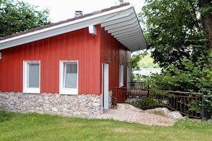 A red building with a stone foundation, a small porch, and a metal fence.