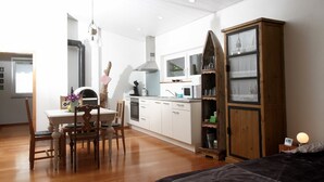 Une cuisine compacte avec des meubles blancs, une table à manger avec des chaises, un meuble en bois et une fenêtre.