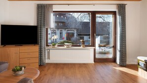 A living room with a TV, wooden cabinets, a radiator, and a window with curtains. - Apartment 'Mit Terasse 110qm' with Mountain View, Private Terrace and Wi-Fi (Schluchsee)