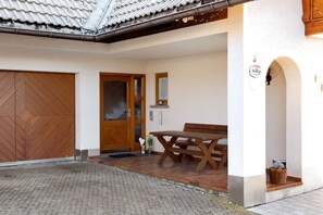 Un espace extérieur abrité, avec un banc et une table en bois, un toit recouvert de tuiles et une porte en bois.