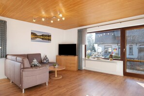 A modern living room with a sofa, TV, wooden flooring, and a large window with a view of a building.