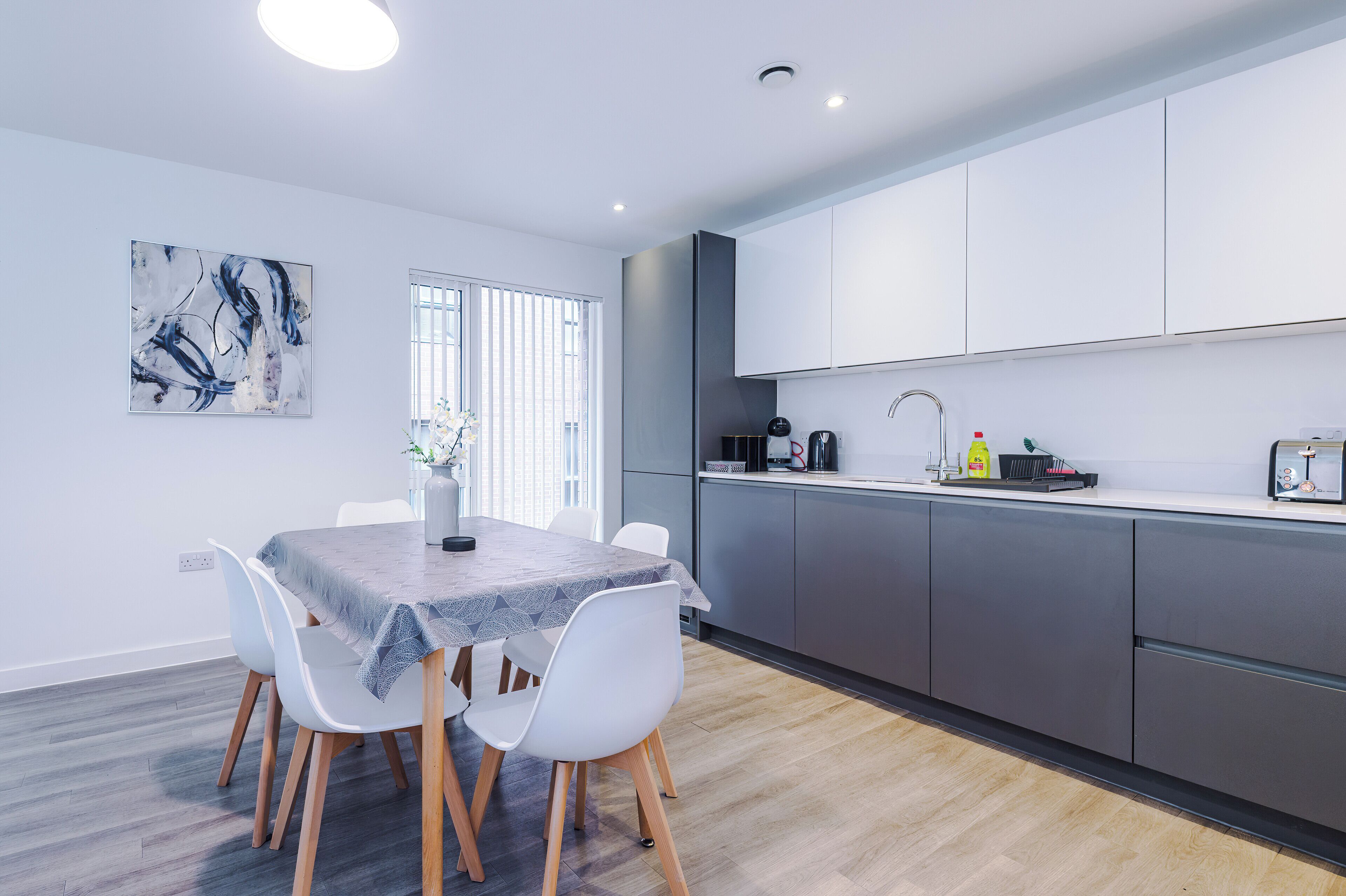 A modern kitchen with grey cabinets, a white countertop, and a dining area with a table and chairs.