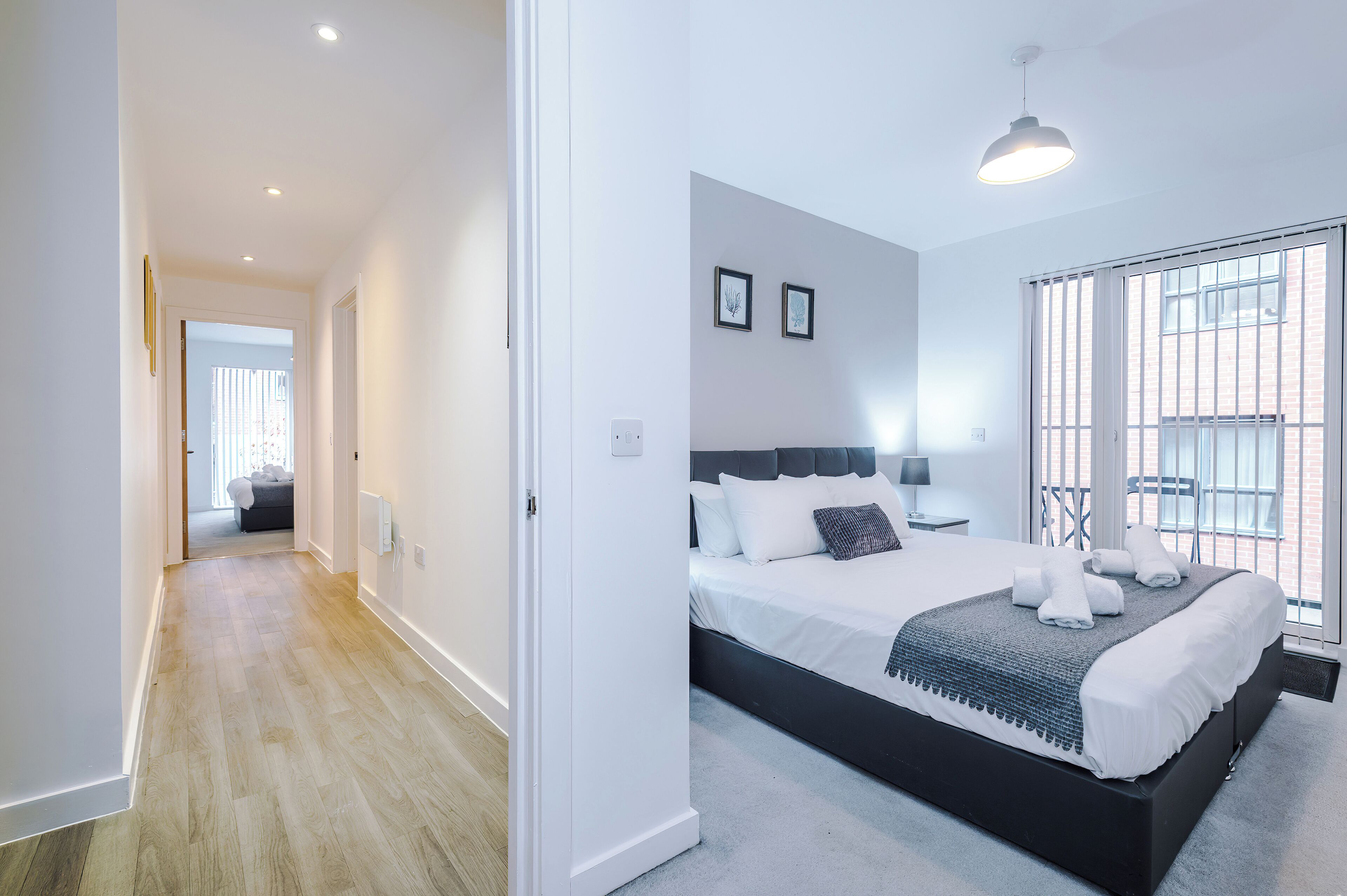 A modern bedroom with a large bed, a view through a window, and a hallway leading to another room.