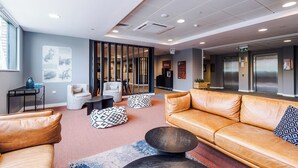 A modern lobby with a leather sofa, a coffee table, and a patterned rug. There is a reception desk with a computer and a vase. - 2 Bedroom Duplex Apartment (Sheffield)