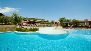 A large outdoor swimming pool with lounge areas and umbrellas, surrounded by greenery and buildings. - Three-room Apartment With Pool (Villasimius)