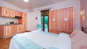 A bedroom with a bed, a small kitchenette, and a door leading to a balcony. - Three-room Apartment With Pool (Villasimius)