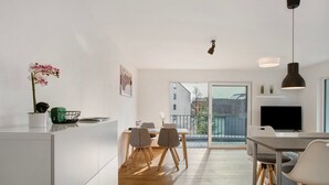 A modern kitchen with a dining area, wooden flooring, and a large window offering a view of buildings.