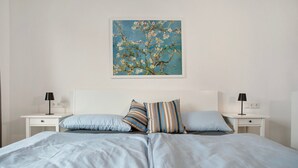 A bedroom with a large bed, two bedside tables, and a wall-mounted painting of a tree.