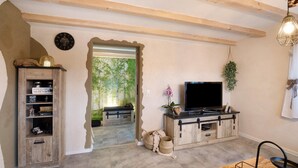 Sala de estar com um aparador de madeira, uma televisão de tela plana, um armário de madeira e uma janela grande com vista para área verde.