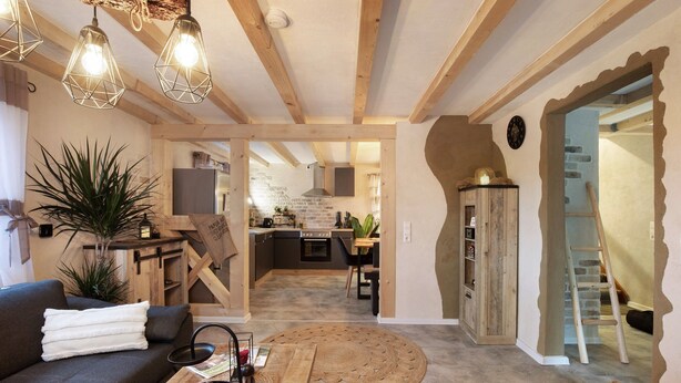 Uma sala aconchegante com sofá, mesa de centro e mesa de jantar. Uma cozinha é visível ao fundo.