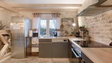 Cocina compacta con lavavajillas integrado, refrigerador de acero inoxidable, estufa y ventana con cortinas.