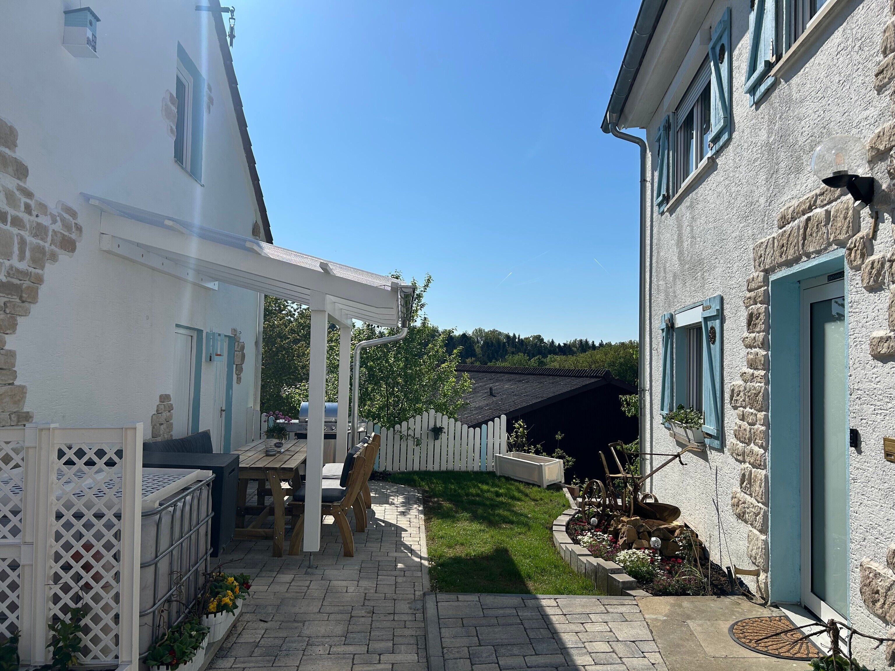 En patio med pergola, grill og et hvidt hegn.