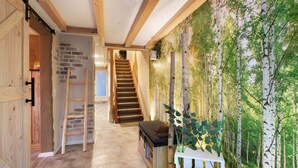 Interior em madeira com escada, um banco e um mural na parede retratando uma floresta.