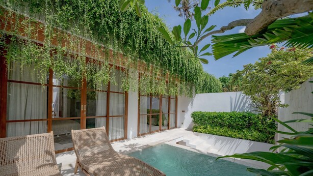Ein Poolbereich mit Korlounge-Stühlen, einem Wintergarten und üppiger Bepflanzung.