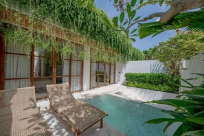 A pool area with wicker lounge chairs, a glass-enclosed room, and lush greenery. - Villa Tana Pererenan (Canggu)