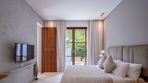 Ein modernes Schlafzimmer mit einem großen Bett, einem Flachbildfernseher und Blick auf Grünflächen durch eine Glastür.